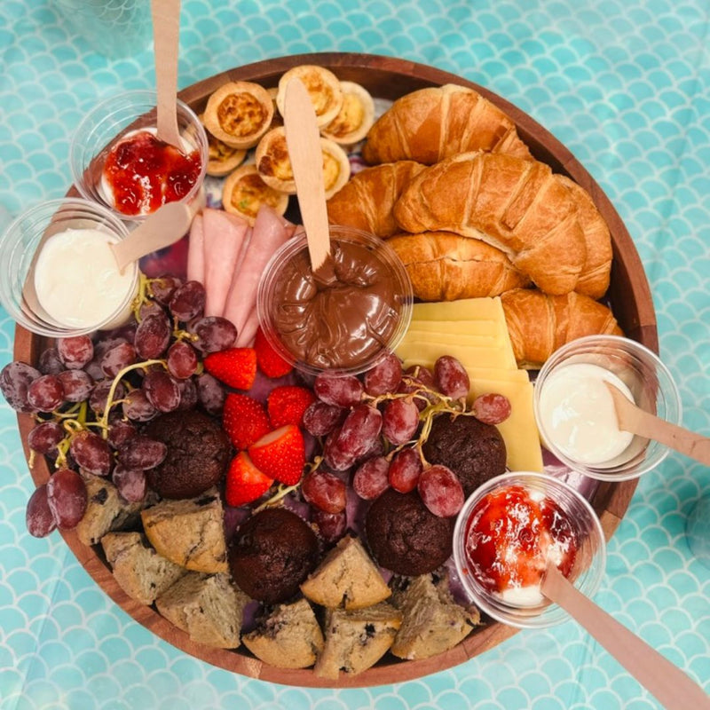 DIY Invasion's catering called Grazing Platters featuring assorted foods including croissants, fruits, and spreads on a blue patterned surface.
